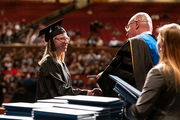 Graduates walk across the stage and accept their diploma.