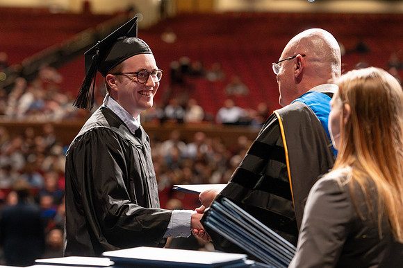 Graduates walk across the stage and accept their diploma.