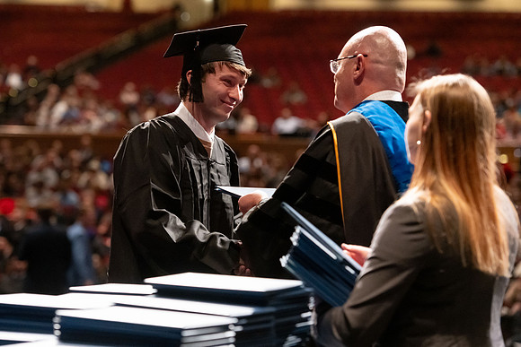 Graduates walk across the stage and accept their diploma.