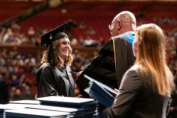 Graduates walk across the stage and accept their diploma.