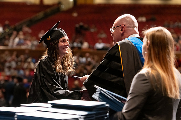 Graduates walk across the stage and accept their diploma.