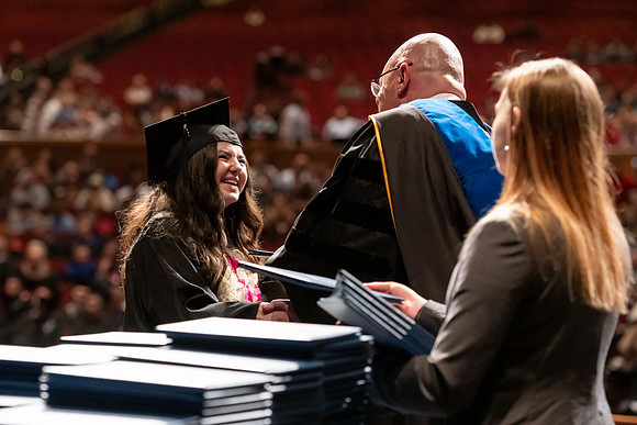 Graduates walk across the stage and accept their diploma.