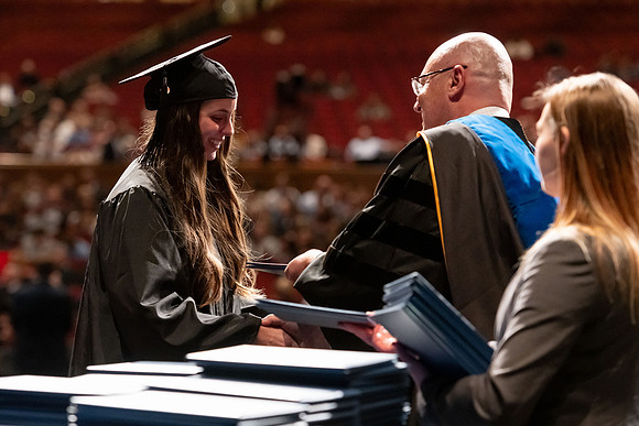Graduates walk across the stage and accept their diploma.