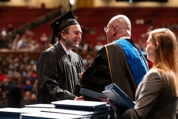 Graduates walk across the stage and accept their diploma.