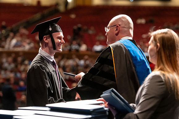 Graduates walk across the stage and accept their diploma.