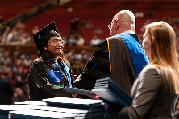 Graduates walk across the stage and accept their diploma.