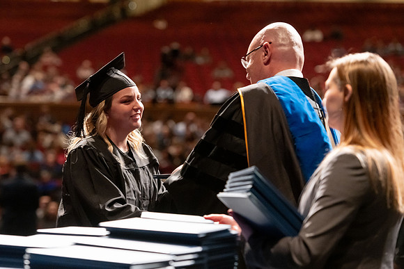 Graduates walk across the stage and accept their diploma.