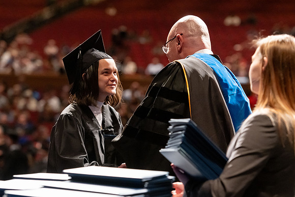 Graduates walk across the stage and accept their diploma.