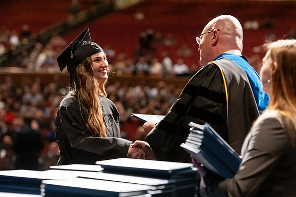 Graduates walk across the stage and accept their diploma.