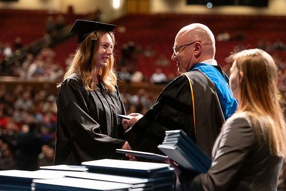Graduates walk across the stage and accept their diploma.