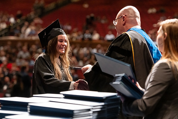 Graduates walk across the stage and accept their diploma.