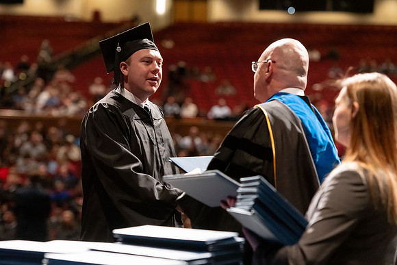 Graduates walk across the stage and accept their diploma.