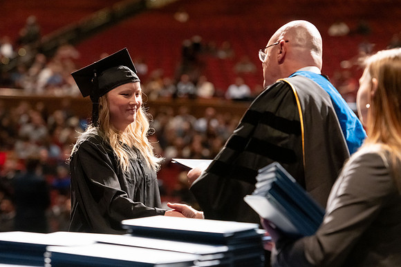 Graduates walk across the stage and accept their diploma.
