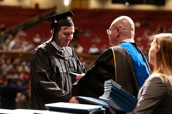 Graduates walk across the stage and accept their diploma.
