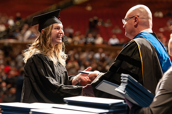 Graduates walk across the stage and accept their diploma.