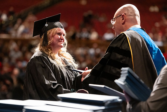 Graduates walk across the stage and accept their diploma.