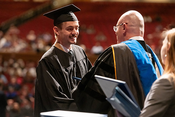 Graduates walk across the stage and accept their diploma.