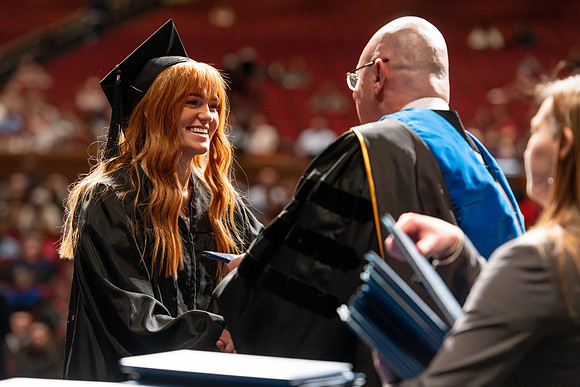 Graduates walk across the stage and accept their diploma.