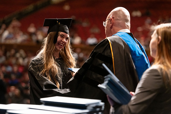 Graduates walk across the stage and accept their diploma.