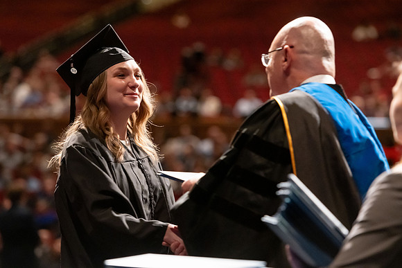 Graduates walk across the stage and accept their diploma.