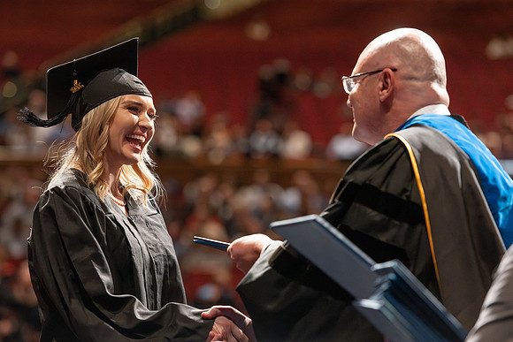 Graduates walk across the stage and accept their diploma.