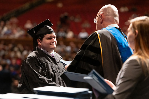 Graduates walk across the stage and accept their diploma.