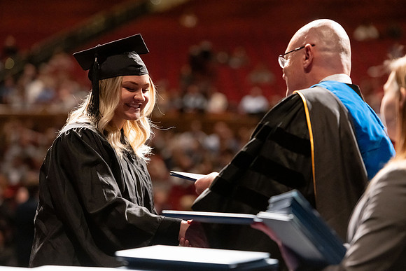 Graduates walk across the stage and accept their diploma.