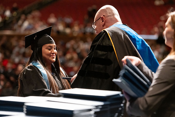 Graduates walk across the stage and accept their diploma.