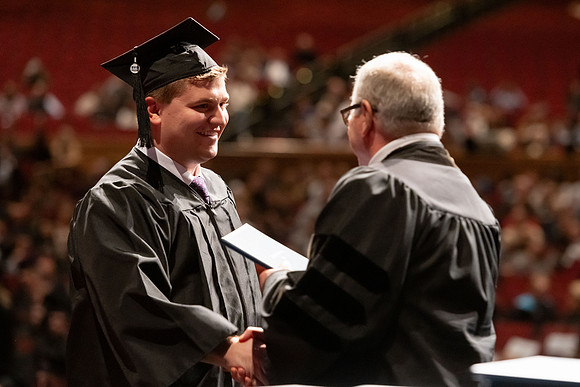 Graduates walk across the stage and accept their diploma.