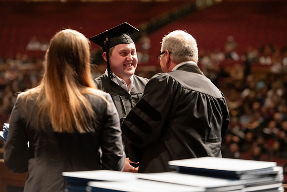 Graduates walk across the stage and accept their diploma.