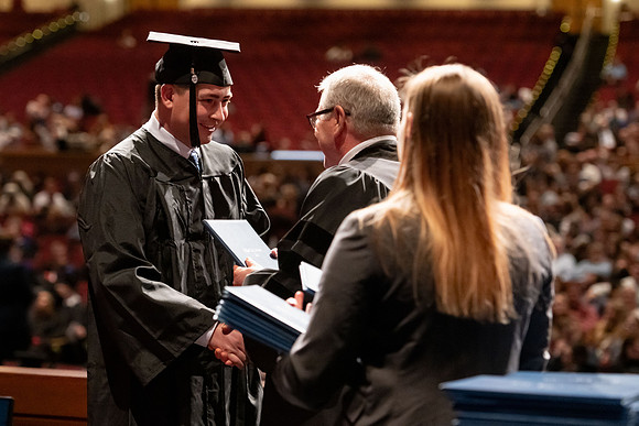 Graduates walk across the stage and accept their diploma.