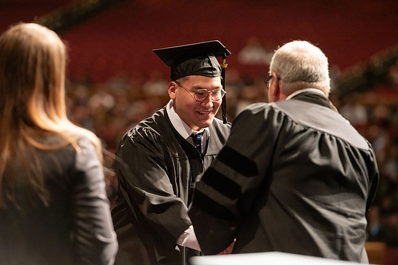 Graduates walk across the stage and accept their diploma.