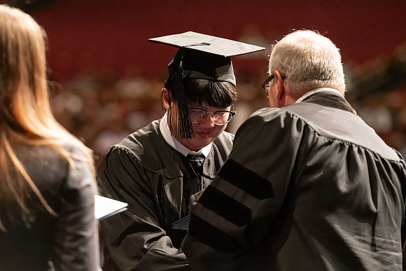 Graduates walk across the stage and accept their diploma.