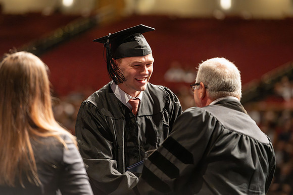 Graduates walk across the stage and accept their diploma.