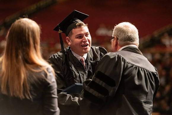 Graduates walk across the stage and accept their diploma.