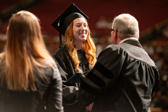 Graduates walk across the stage and accept their diploma.