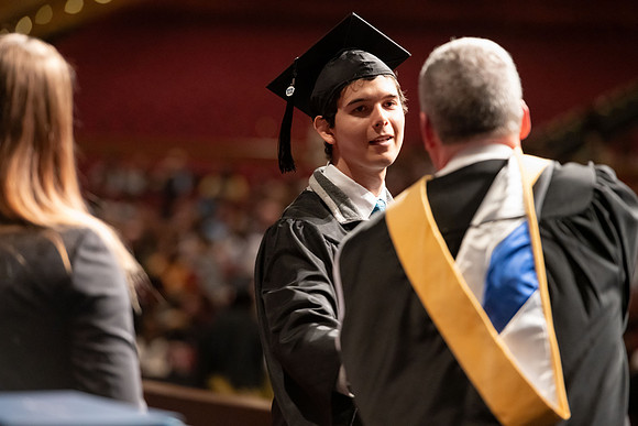 Graduates walk across the stage and accept their diploma.