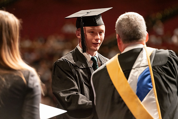 Graduates walk across the stage and accept their diploma.