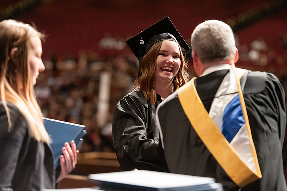 Graduates walk across the stage and accept their diploma.