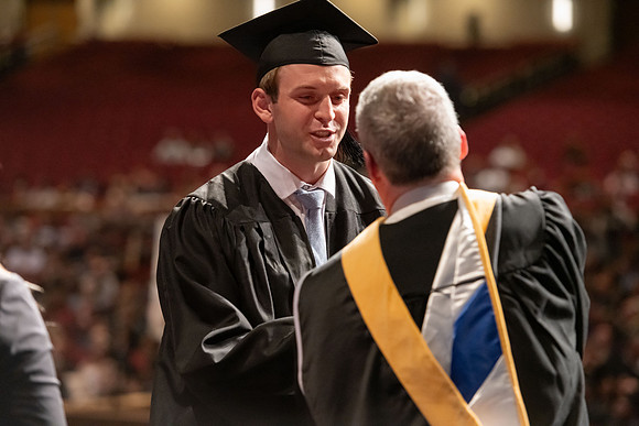 Graduates walk across the stage and accept their diploma.