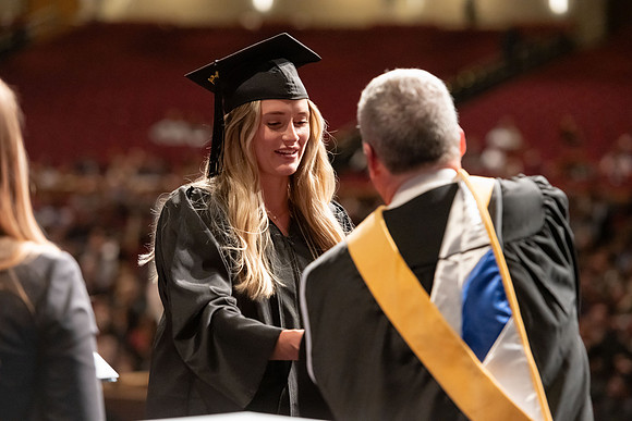 Graduates walk across the stage and accept their diploma.
