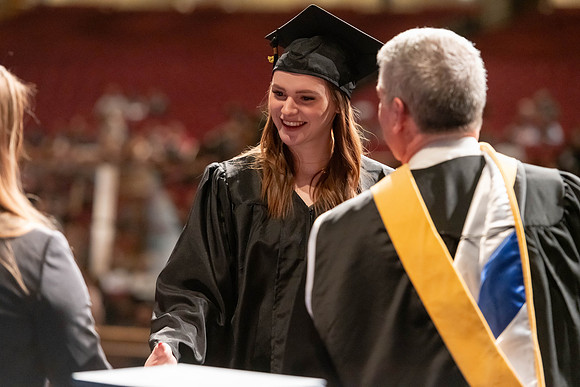 Graduates walk across the stage and accept their diploma.