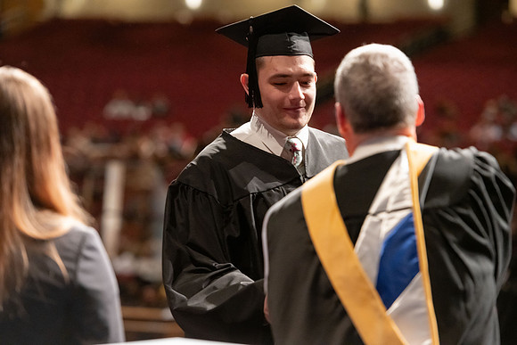 Graduates walk across the stage and accept their diploma.