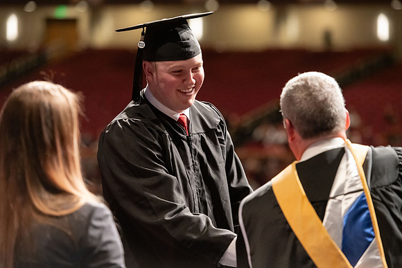 Graduates walk across the stage and accept their diploma.