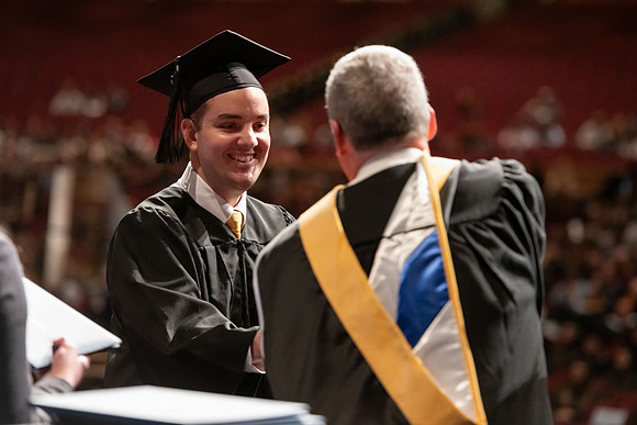 Graduates walk across the stage and accept their diploma.