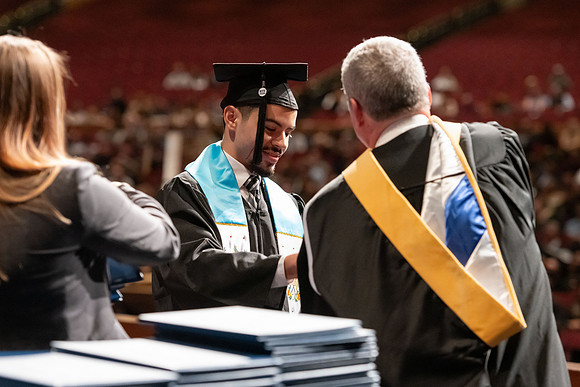 Graduates walk across the stage and accept their diploma.
