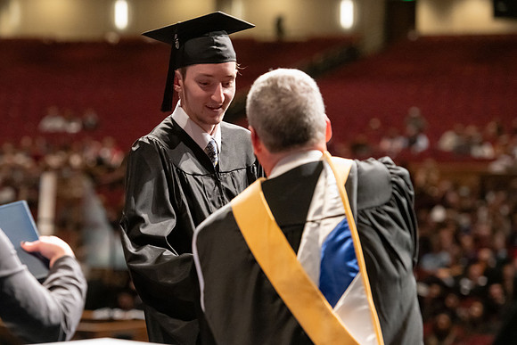Graduates walk across the stage and accept their diploma.