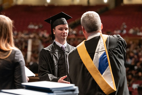 Graduates walk across the stage and accept their diploma.