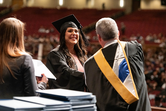 Graduates walk across the stage and accept their diploma.
