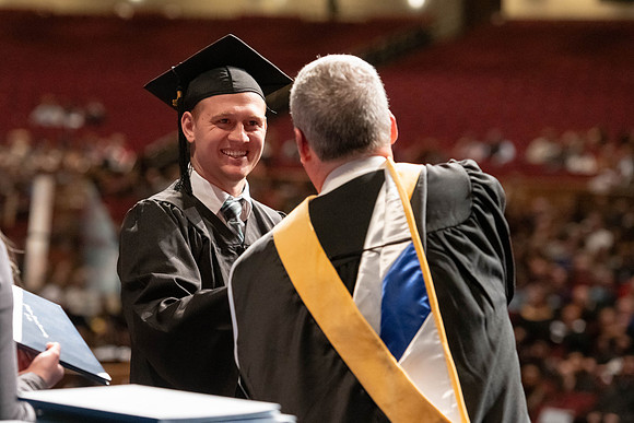 Graduates walk across the stage and accept their diploma.